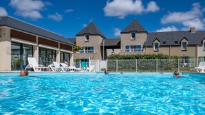 Una piscina con sillas de descanso, un edificio de fachadas de piedra y un cielo azul despejado.