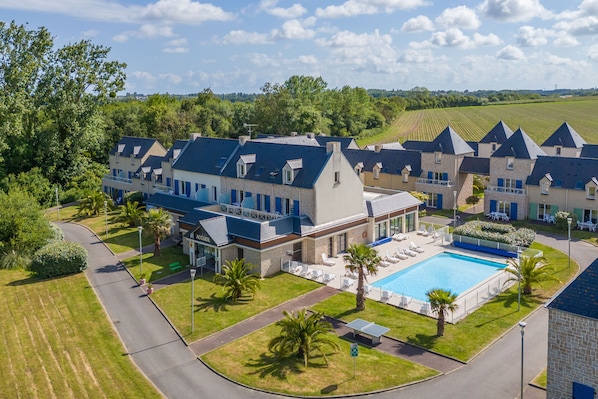 A hotel with a swimming pool, multiple buildings, and a landscaped area with palm trees.