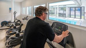 A man using a treadmill in a gym with a view of a pool and outdoor seating area.