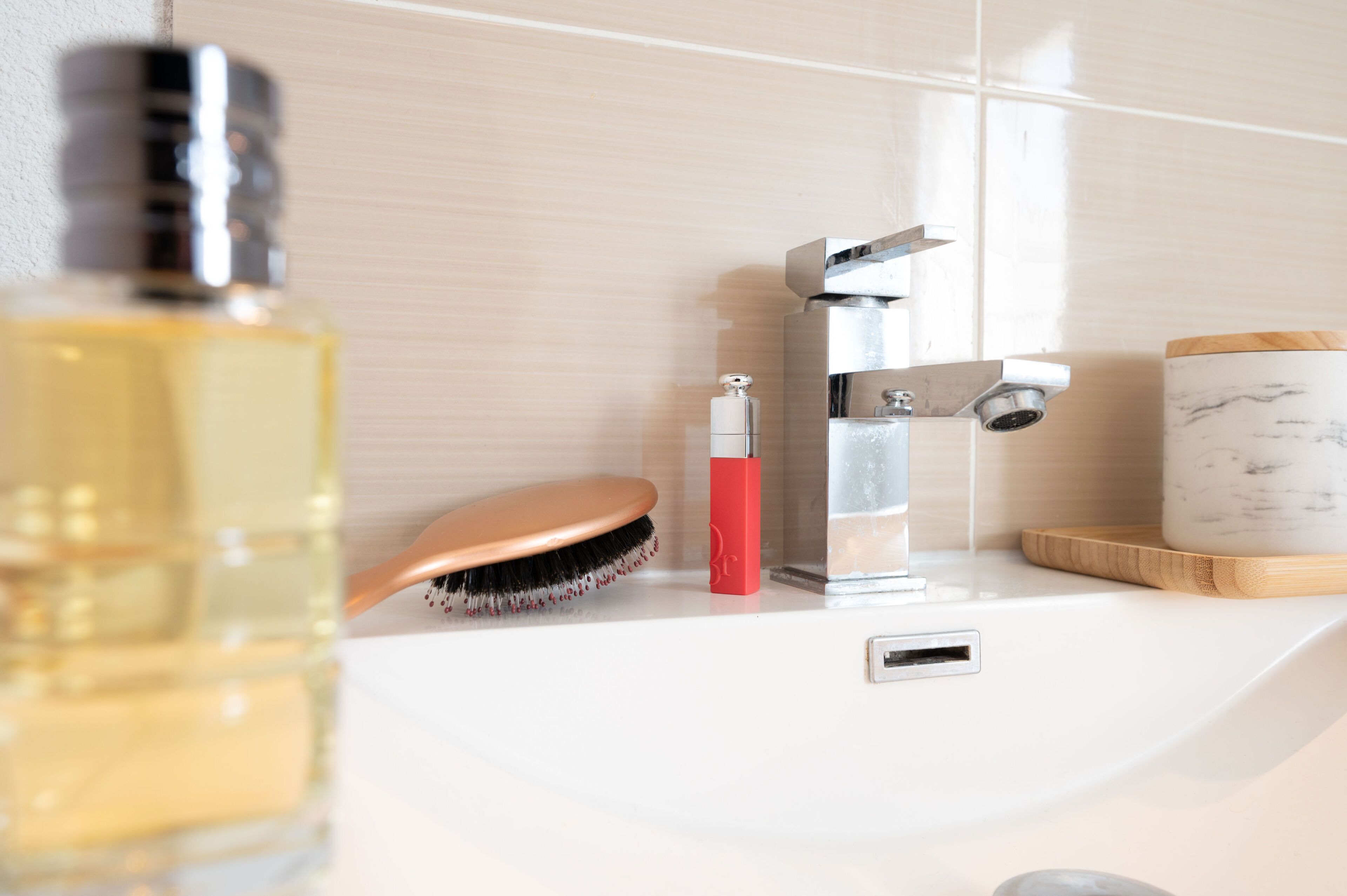 A bathroom with a white sink, a mirror, a bottle of liquid, a red soap dispenser, and a wooden tray.