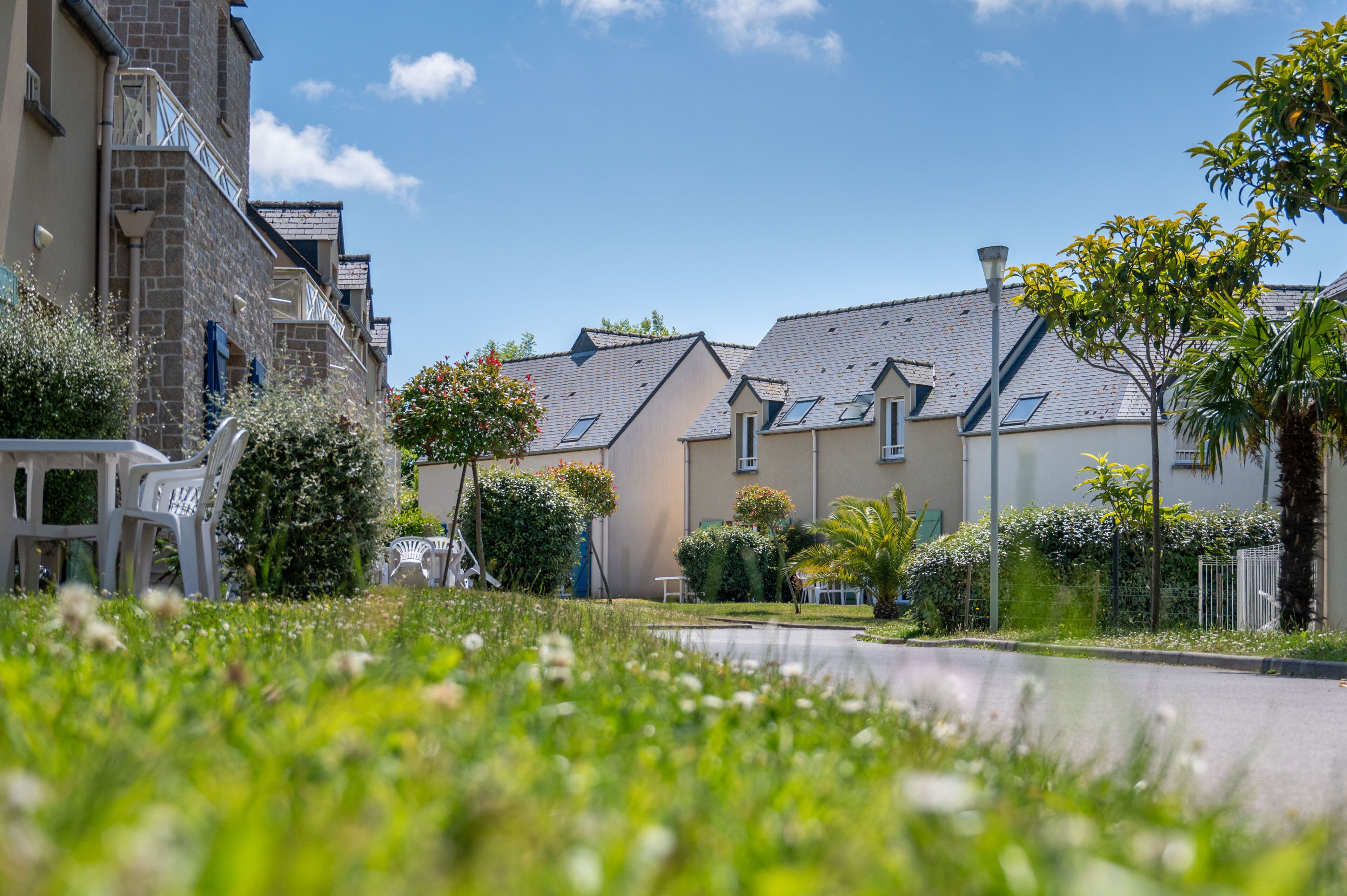 Une rue résidentielle bordée de maisons, avec un ciel dégagé et une zone herbeuse.