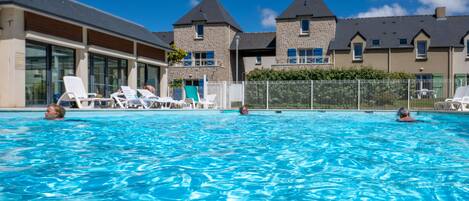 En swimmingpool med solstolar, en byggnad med fasader i sten och en klarblå himmel.