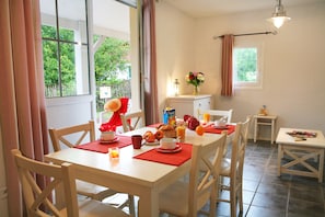 Un coin repas avec une table mise pour le petit-déjeuner, des chaises, une fenêtre avec des rideaux et une petite table avec une lampe.