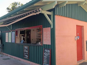 Un petit bâtiment à l’extérieur vert et à la porte rouge, où l’on peut voir un menu de pizzas et une enseigne indiquant un service de livraison à domicile.