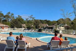 Une piscine entourée d’arbres et de bâtiments, avec des chaises longues et des parasols.