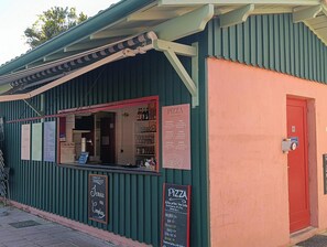 Un petit bâtiment à l’extérieur vert et à la porte rouge, où l’on peut voir un menu de pizzas et une enseigne indiquant un service de livraison à domicile.