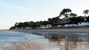 Uma praia com um prédio branco, árvores e céu claro.