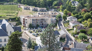 A multi-story hotel with balconies, a parking lot, and a vineyard in the background.