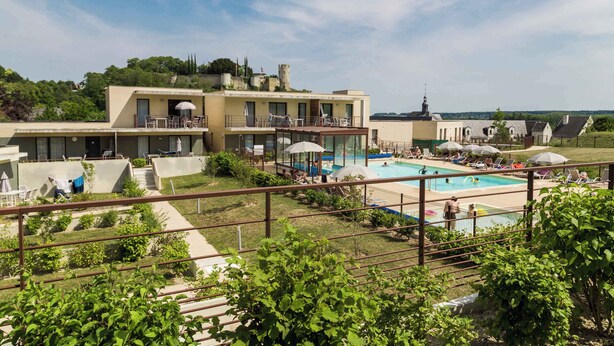A hotel with a swimming pool, outdoor seating, and a view of the surrounding landscape.