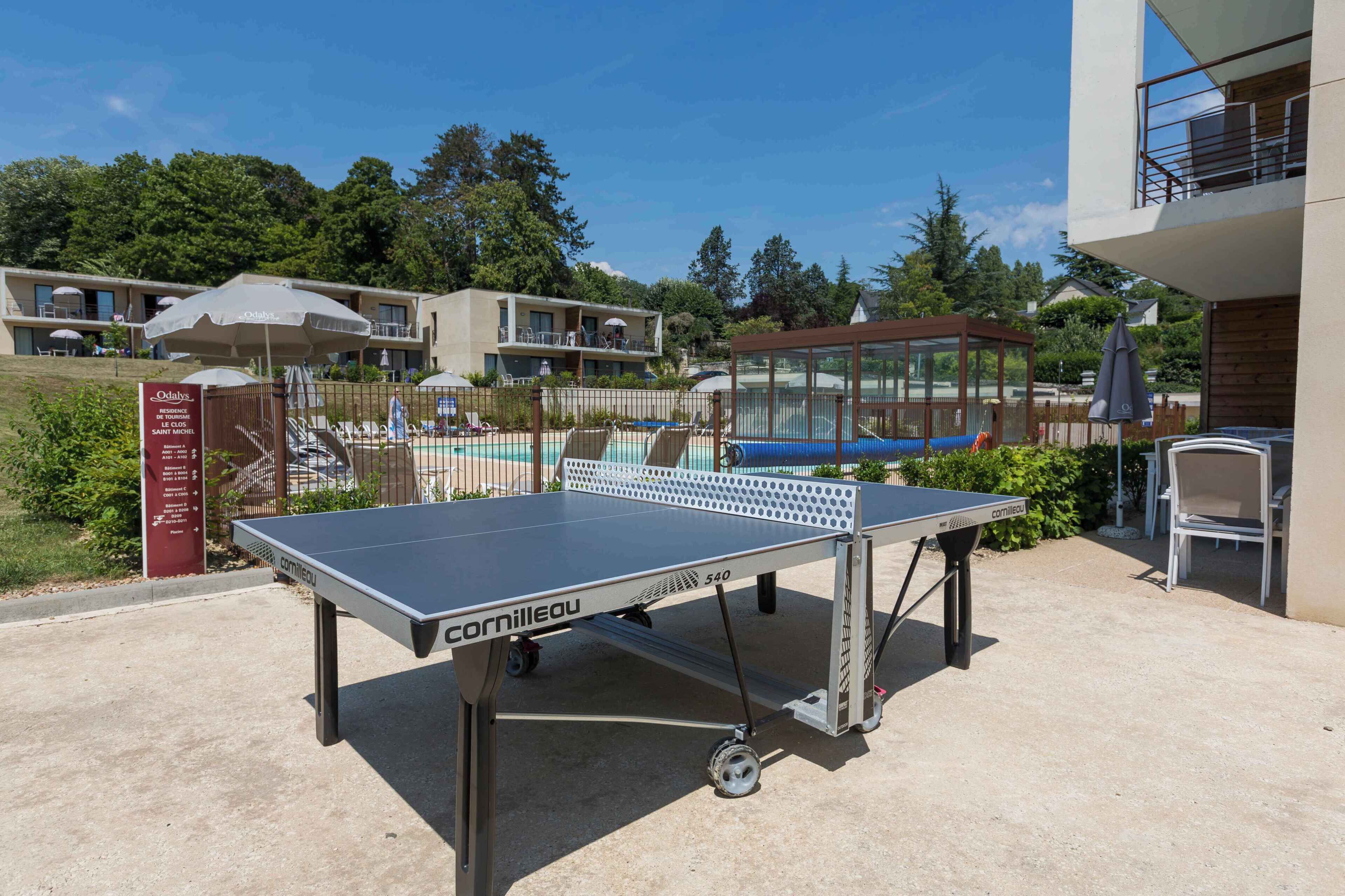 A ping pong table in an outdoor area with a pool and a building in the background.