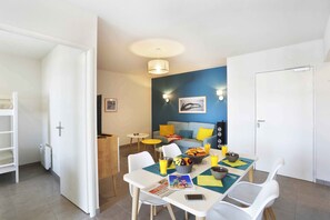 A dining area with a table set for two, a basket of fruit, and a bowl of cereal.