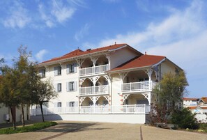 A multi-story building with balconies, a red roof, and a white facade.