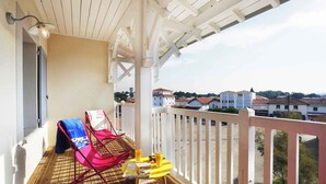 A balcony with a wooden floor, a white railing, a pink chair, a yellow table, and a bottle of orange juice. - À proximité de la plage | Salle fitness | Balcon (Mimizan)