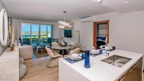 A modern kitchen with a central island, dining area with chairs, and a large window with a view. - Luxury Apartment with stunning ocean views and pool (St. George)