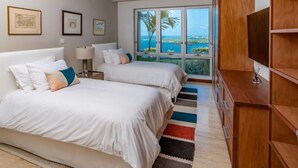 A hotel room with two beds, a large window with a view, a wooden cabinet, and a framed picture on the wall. - Luxury Apartment with stunning ocean views and pool (St. George)
