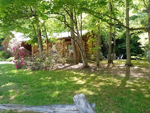 A rustic log cabin with a stone foundation, surrounded by a well-maintained lawn and trees. - Riverside Serenity: Modern Log Cabin on a Private Trout Stream (Mars Hill)