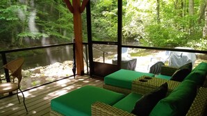 Ein Zimmer mit Holzterrasse, Korbmöbeln und Blick auf eine bewaldete Landschaft.