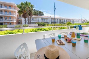 Un balcon avec une table dressée pour le dîner, comprenant un chapeau, des boissons et des fruits.