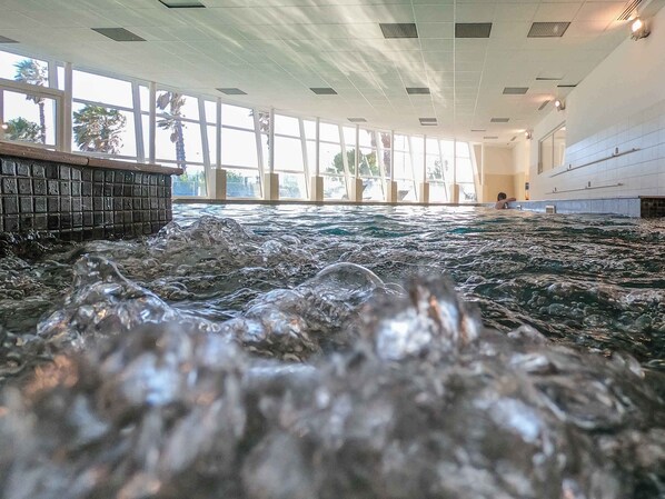 Une grande piscine intérieure à l’eau claire, entourée d’un haut plafond et de grandes fenêtres.