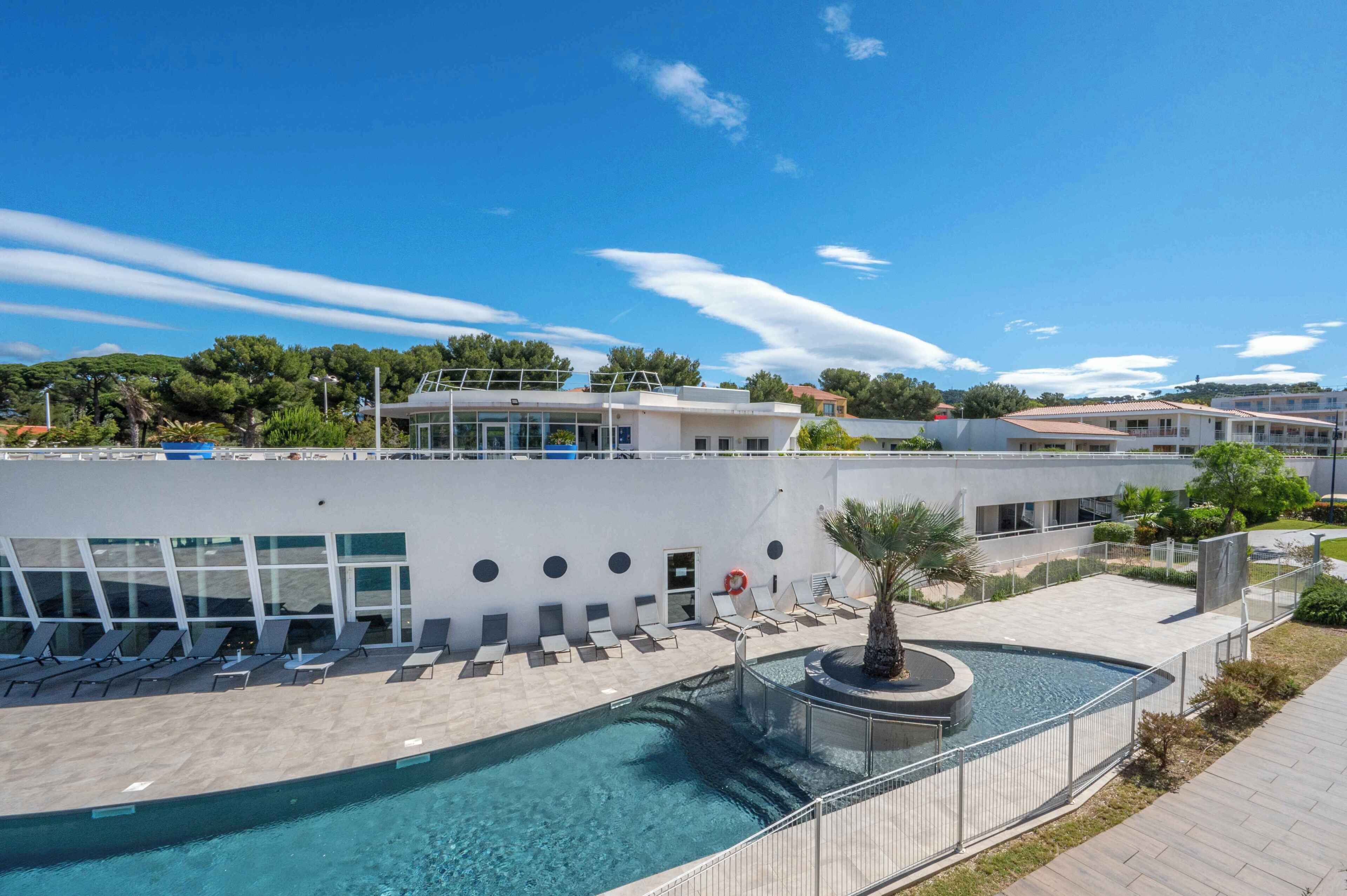 Et poolområde med liggestole, en rund pool og en bygning med moderne arkitektur.