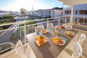 Varanda com mesa posta para refeição, vista para uma rua e edifícios.