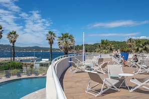 Ein Poolbereich mit Liegestühlen, einem Pool und Blick auf das Meer und die Hügel.