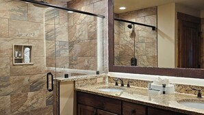 Un baño con ducha, un espejo grande y un tocador con lavamanos y cajones de almacenamiento.