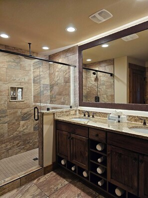 A bathroom with a shower, a large mirror, and a vanity with a sink and storage drawers. - Beautiful 1-bedroom; King, pet friendly, with waterpark included. (Gatlinburg)