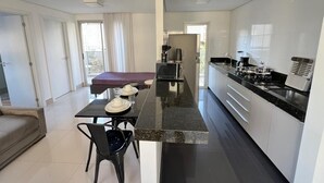 Moderni keittiö, jossa on keskeinen saareke, oleskelutila ruokailuryhmällä ja näkymä ulos.