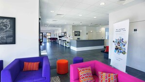 A modern lobby with purple and pink seating, a reception desk, and a poster on the wall.