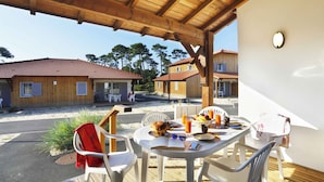 A covered outdoor dining area with a table set for two, chairs, and a view of nearby buildings.