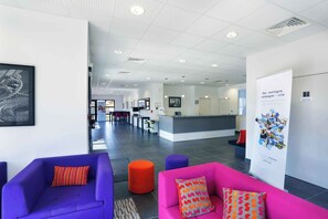 Een moderne lobby met paars en roze zitplaatsen, een receptiebalie en een poster aan de muur.