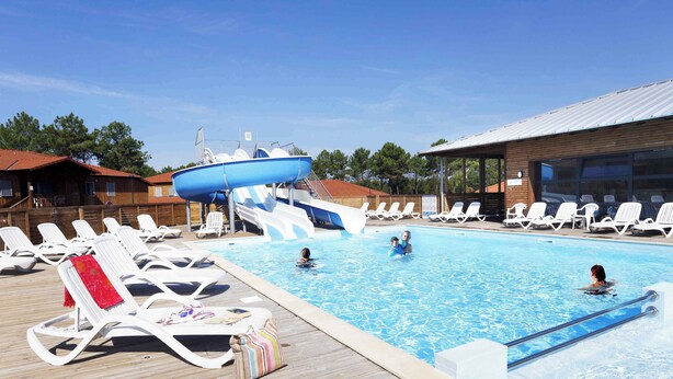 Zona de piscina con sillas de descanso, un tobogán y una terraza de madera.