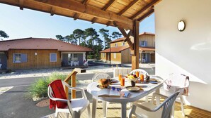 Un área de comedor al aire libre techada con una mesa dispuesta para dos, sillas y vistas de edificios cercanos.