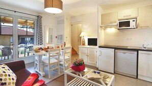 Una cocina moderna con armarios blancos, microondas y lavavajillas. Cuenta con un comedor con mesa y sillas, además de una sala de estar con sofá y una mesa de centro.