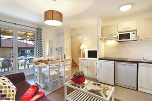A modern kitchen with white cabinets, a microwave, and a dishwasher. There is a dining area with a table and chairs, and a living area with a sofa and a coffee table.