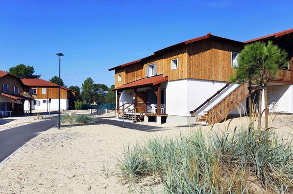 A coastal building with a wooden exterior, a balcony, and a staircase leading to the entrance.