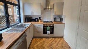 Eine kleine Küche mit weißen Schränken, einer Holz Arbeitsplatte, einem eingebauten Backofen und einem Fenster mit Blick auf ein Backsteingebäude.