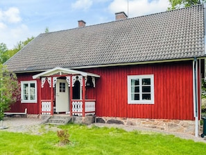 A red wooden house with a tiled roof, a porch with white railings, and a stone foundation. - 6 Person Holiday Home in Almhult (Almhult)