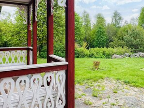 A wooden deck with intricate white railings, a stone pathway, and a lush green garden with trees and shrubs. - 6 Person Holiday Home in Almhult (Almhult)