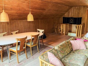 Un intérieur en bois avec une table de salle à manger ronde, des chaises, un canapé agrémenté de coussins à motifs et des lampes suspendues.