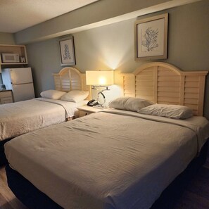 A hotel room with two beds, a bedside table with a lamp, a phone, and a microwave on a cabinet. - Oceanfront Efficiency T1008 (Myrtle Beach)
