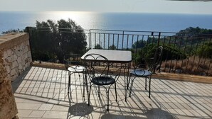 Un patio con una mesa y sillas, un muro de piedra y vista al mar.