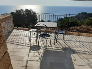 Eine Terrasse mit Tisch und Stühlen, eine Steinsäule und Meerblick.