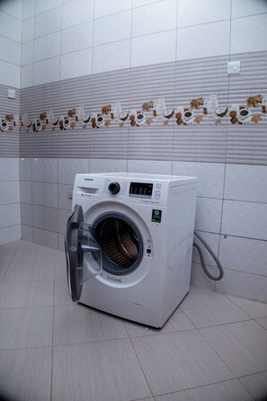 A front-loading washing machine in a bathroom with tiled walls and a decorative leaf pattern. - 3 BEDROOMS SELF CONTAINED HOUSE IN KIMARA DAR ES SALAAM TANZANIA, ERGONOMIC BEDS (Temboni KIMARA B DAR ES SALAAM)