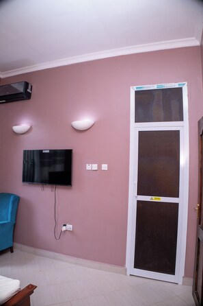 Ein Zimmer mit an der Wand montiertem Fernseher, einer Tür mit Fenster und einer Steckdose.