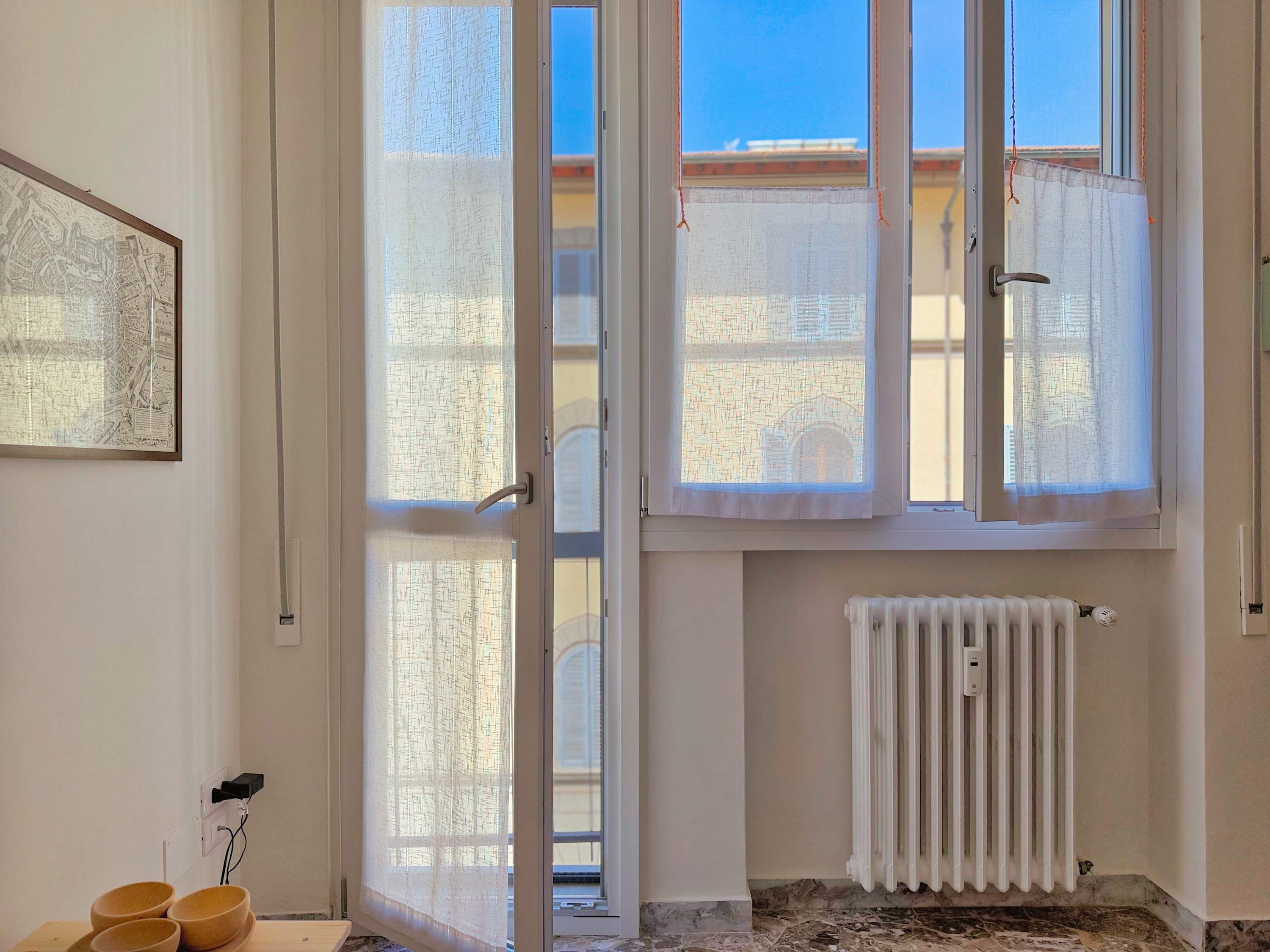 A room with a large window, a radiator, and a framed map on the wall.