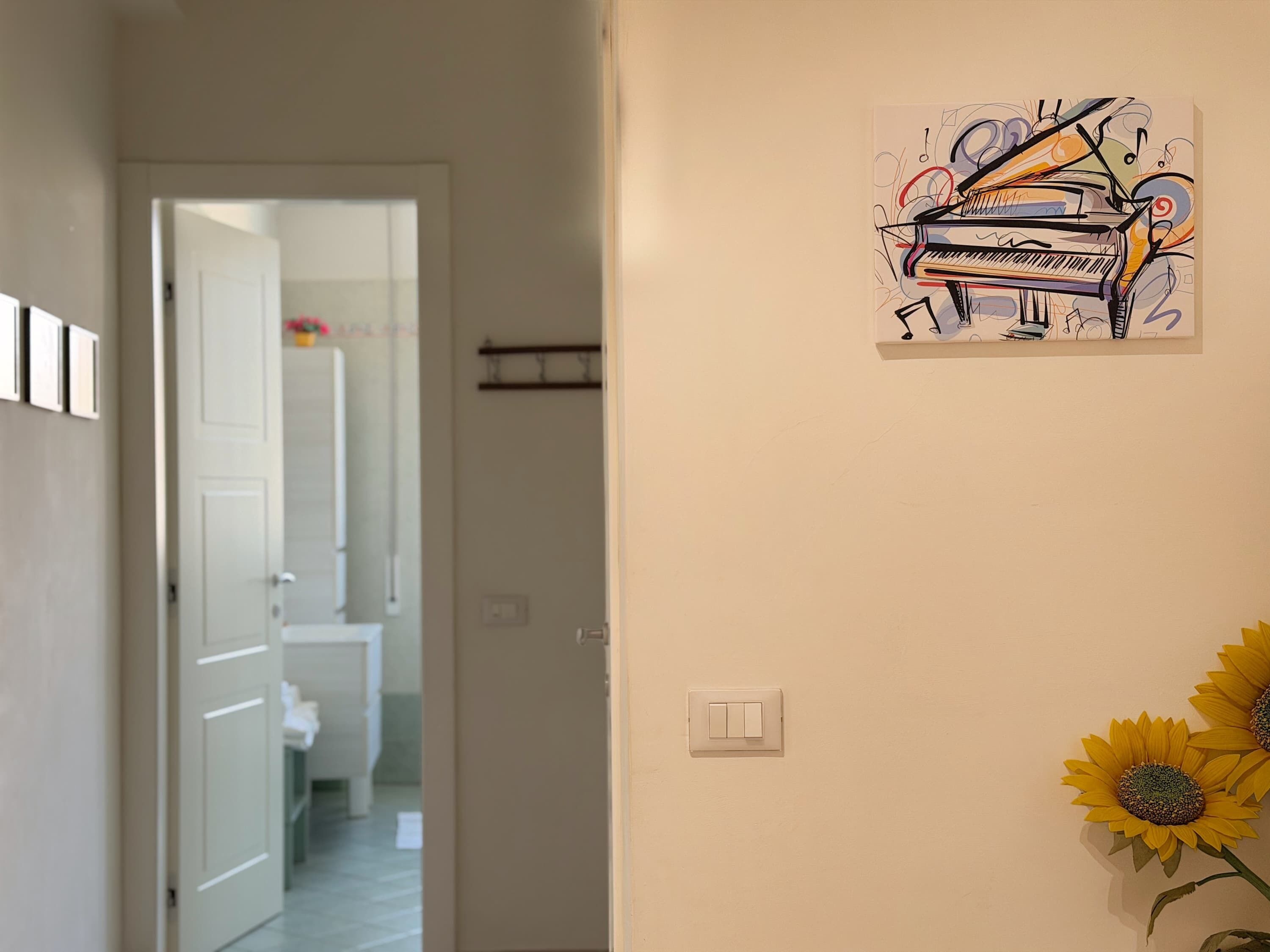 A hallway with a door leading to a bathroom, a light switch, and a wall-mounted artwork of a piano.