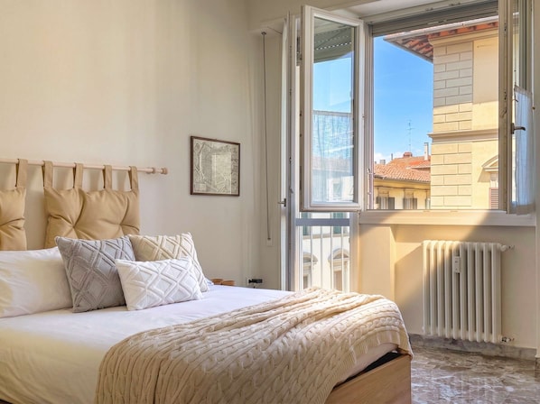 A bedroom with a bed, pillows, a radiator, and a window with an open door. - Il Pianoforte, authentic with balcony (Firenze)