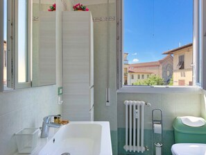 Ein Badezimmer mit Badewanne, Toilette, Heizkörper und einem Fenster mit Blick auf Gebäude.